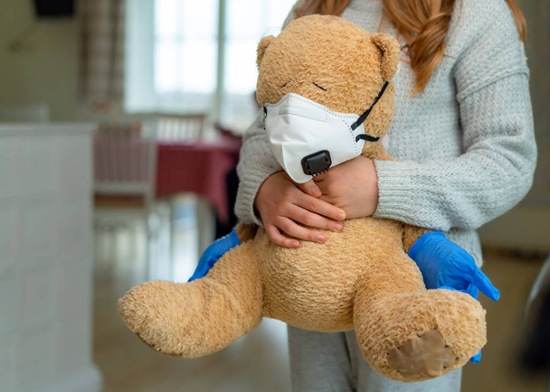 Teenage girl hugging teddy bear with face mask. Concept of corona virus, staying at home, isolation. Preventing flu virus - Foto, Imagen