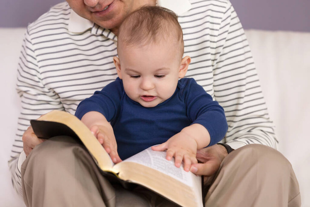 Grandad reading stories from the Holy Bible to his young grandson - 写真・画像