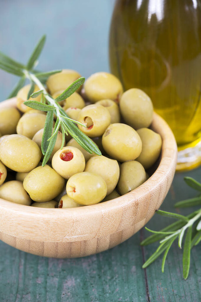 Fresh healthy green olives with rosemary and virgin oil in a bottle on wooden table - Фото, зображення