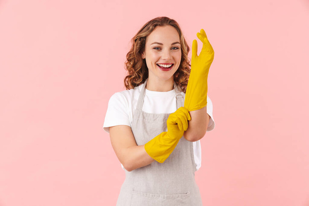 Image of a happy young woman housewife in gloves isolated over pink wall background. - Fotografie, Obrázek
