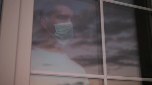 Droevige man met een medisch masker kijkt naar het raam. 4K - Video