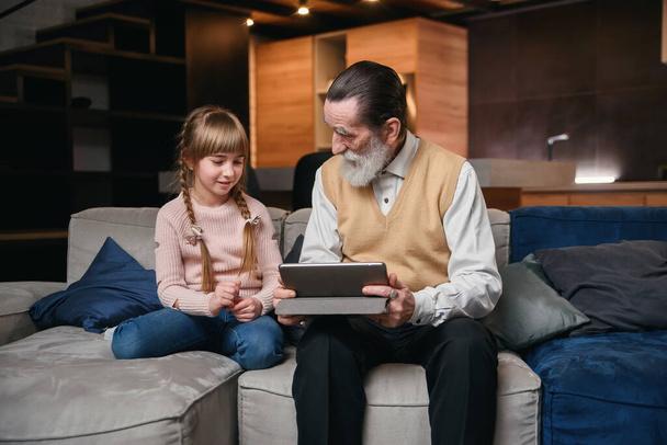 Grandpa with his granddaughter using tablet at cozy home. - Foto, immagini