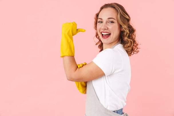 Bild von glücklichen positiven Frau Hausfrau isoliert über rosa Wand Hintergrund in Handschuhen zeigt Bizeps. - Foto, Bild