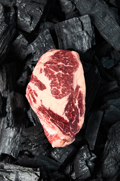 top view of fresh raw steak on black coals - Фото, изображение