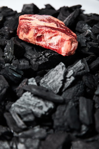 selective focus of fresh raw steak on black coals on white background - Photo, Image