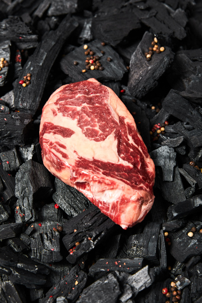 vista superior de filete fresco crudo sobre carbones negros con granos de pimienta
 - Foto, Imagen