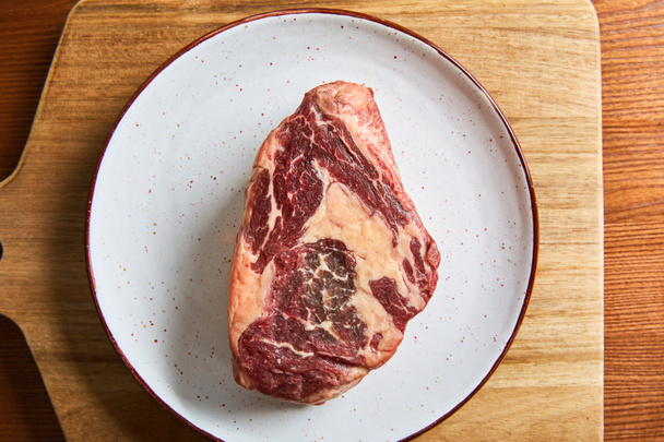 top view of fresh raw steak on plate on cutting board on wooden table - Фото, зображення