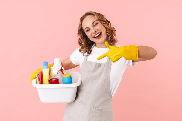 Photo of happy emotional positive woman housewife isolated over pink wall background in gloves holding cleansers. - Foto, immagini
