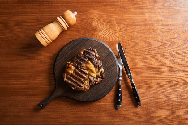 Güvertede taze ızgara biftek, çatal bıçak takımı ve ahşap masada tuz değirmeni. - Fotoğraf, Görsel
