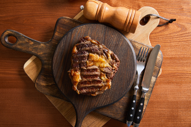Blick von oben auf leckeres Steak vom Grill, serviert auf Holzbrettern mit Besteck, Salz- und Pfeffermühlen - Foto, Bild