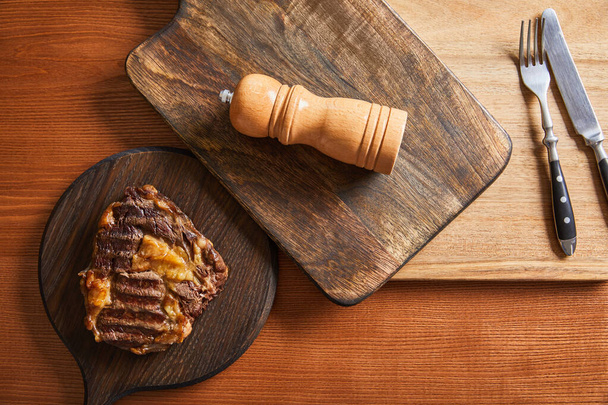 top view of tasty grilled steak served on wooden boards with cutlery and salt mil - Photo, Image