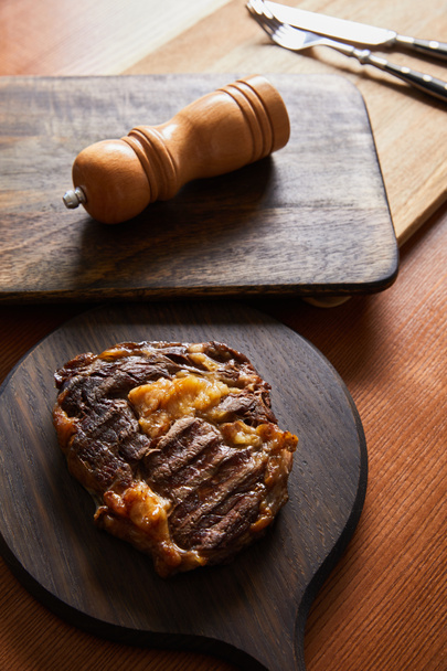 selective focus of tasty grilled steak served on wooden boards with cutlery and salt mil - Фото, изображение