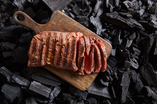 top view of cut fresh grilled tasty steak with rare roasting on wooden cutting board on black coals - Photo, Image