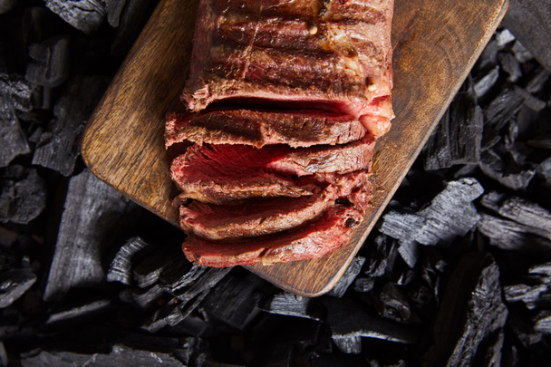 top view of cut fresh grilled tasty steak with rare roasting on wooden cutting board on black coals - Фото, зображення