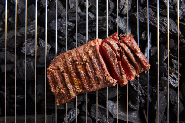 top view of cut fresh grilled tasty steak with rare roasting on grate above black coals - Foto, immagini