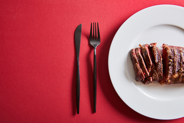 Kırmızı arka planda çatal bıçakla servis edilen lezzetli ızgara bifteğin üst görüntüsü. - Fotoğraf, Görsel