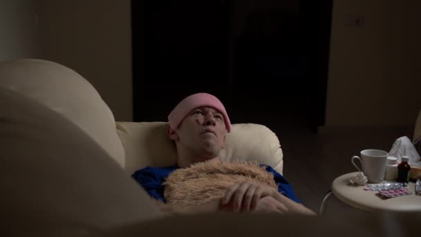Ein kranker junger Mann liegt auf der Couch und misst die Temperatur - Filmmaterial, Video