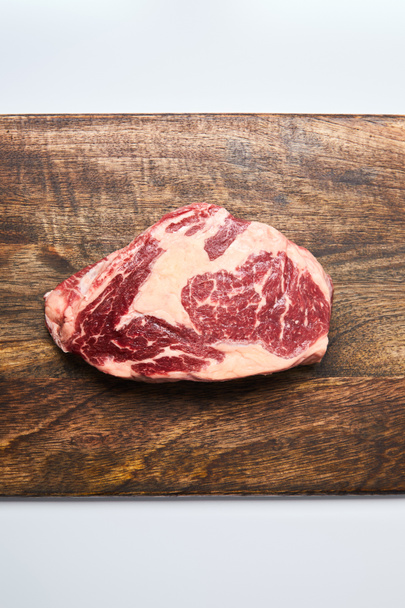 top view of fresh raw steak on wooden cutting board on white background - Photo, Image