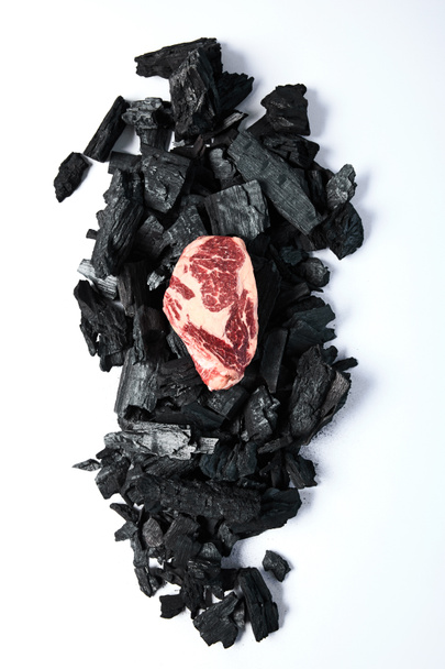 top view of fresh raw steak on black coals on white background - Фото, изображение