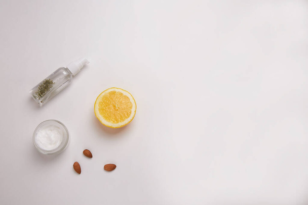 On a white background micellar water, white cream, almonds and a slice of lemon. - Zdjęcie, obraz