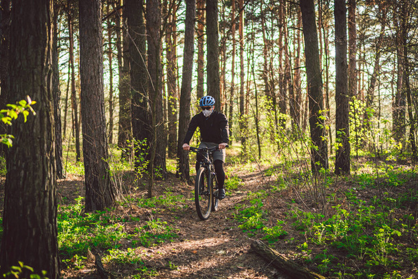 Jongeman fietst in het bos. Een jonge atleet op een fiets in het park. Mannelijke fietser draagt gezichtsmasker, met filter pm 2.5. thema Coronavirus Of Covid 19. Quarantainesport. - Foto, afbeelding