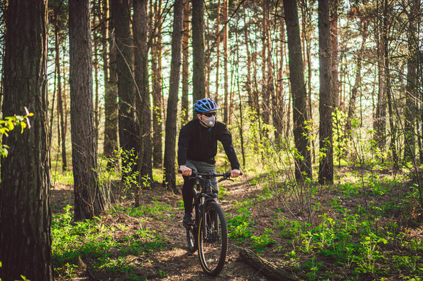 Fiatal férfi védőruhában a környezetszennyezéstől hegyi biciklivel az országúton. Biciklis biciklizik az erdőben. Arcszennyezés maszk szmog por pm2.5 védelem. - Fotó, kép