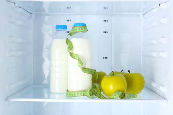 Conceptual photo of diet: apple and milk bottle with measuring type on shelf of refrigerator - Foto, afbeelding