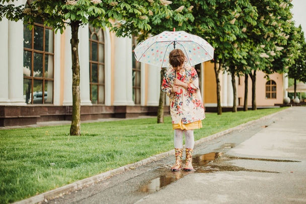 Красивая девушка в яркой дождевой куртке ходит под зонтиком во время дождя на улице. Мягкий фокус Концепция счастливого детства
 - Фото, изображение