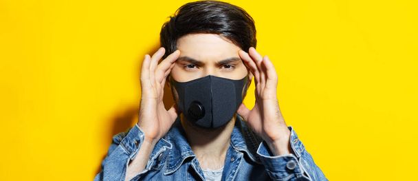 Stúdió portré fiatal fickóról, kezekkel a fején, fekete légzőszervi maszkot visel a koronavírus ellen. Háttér a sárga szín. - Fotó, kép