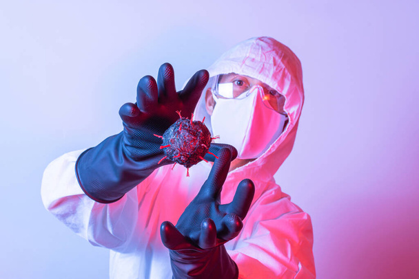 Человек в защитном костюме, защитных очках и маске для борьбы с вирусом Ковид-19 (Корона), пытающийся получить вирусную модель в режиме обеих рук
 - Фото, изображение