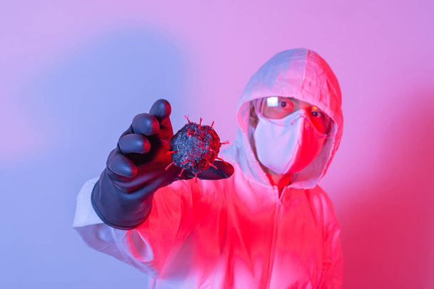 Mann mit Schutzanzug, Schutzbrille und Maske im Kampf gegen Covid-19 (Coronavirus) beim Versuch, ein Virenmodell zu bekommen. Rotes und blaues Licht - Foto, Bild