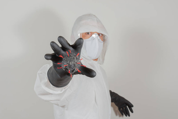 コヴィッド-19(コロナウイルス)と戦うための保護服、ゴーグル、マスクを身に着けている男は、ウイルスモデルを取得しようとしています。隔離。 - 写真・画像
