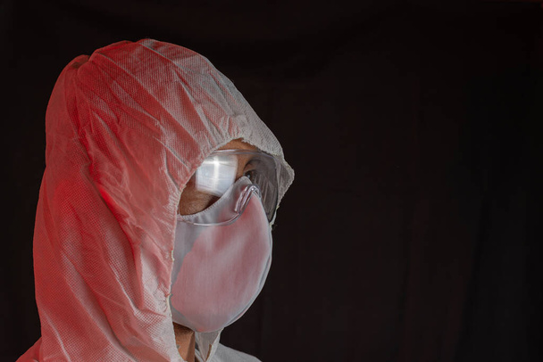 Карантин, коронавирус. Латиноамериканец в халате, защитной маске и очках на черном фоне. Копирование пространства
 - Фото, изображение