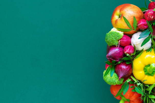 Part of the plant arrangement on the right side of the sheet with radish, red and yellow paprika, broccoli, red onion, apple, garlic  on a green background. Place for text, close up, top view - Photo, Image