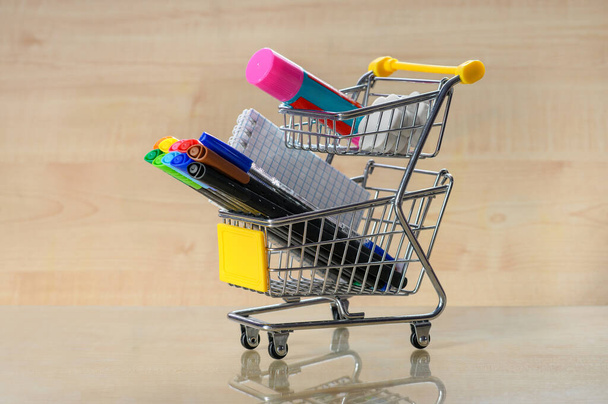 Stationery and shopping cart on a yellow background. Shopping for schoolchildren - Фото, зображення
