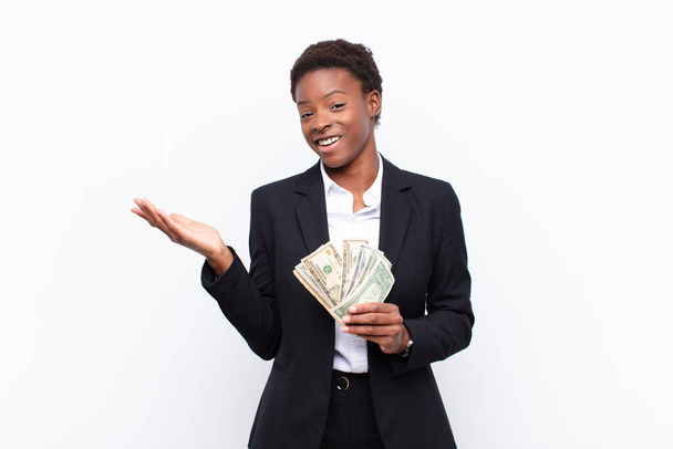 young pretty black womanfeeling happy, surprised and cheerful, smiling with positive attitude, realizing a solution or idea with dollar banknotes - Zdjęcie, obraz