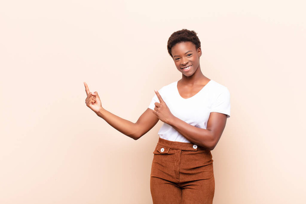 young pretty black womansmiling happily and pointing to side and upwards with both hands showing object in copy space - Foto, imagen