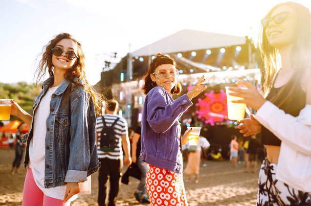Young girlfriends drinking beer and having fun at music festival. Friendship and celebration. Beach party, summer holiday, vacation concept.  - Photo, Image