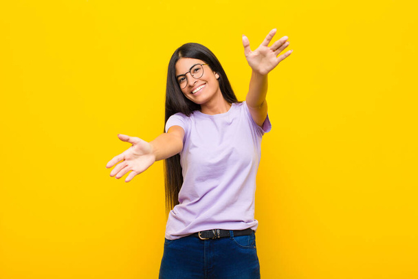 young pretty latin woman smiling cheerfully giving a warm, friendly, loving welcome hug, feeling happy and adorable against flat wall - 写真・画像