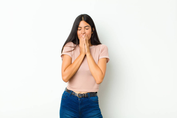 young pretty latin woman happy and excited, surprised and amazed covering mouth with hands, giggling with a cute expression against flat wall - Foto, Imagen