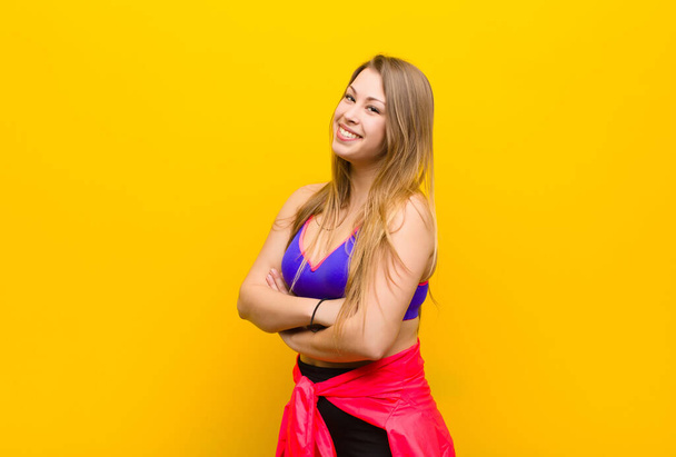 young blonde woman smiling to camera with crossed arms and a happy, confident, satisfied expression, lateral view. sport concept - Фото, зображення