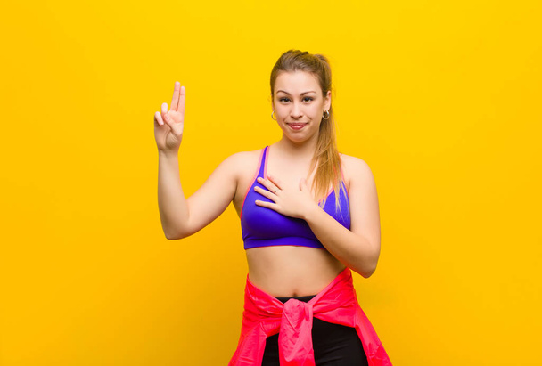 young blonde woman looking happy, confident and trustworthy, smiling and showing victory sign, with a positive attitude. sport concept - Foto, afbeelding
