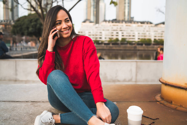Portrait of young latin woman talking on the phone while sitting outdoors. Urban concept. - Foto, Bild