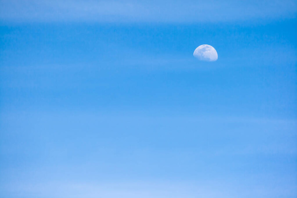 Ciel bleu avec nuages diffus horizontaux et la lune dans sa phase lunaire gibbeuse croissante
 - Photo, image