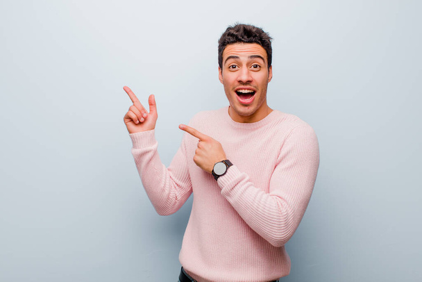 young arabian man feeling joyful and surprised, smiling with a shocked expression and pointing to the side against gray wall - Photo, Image