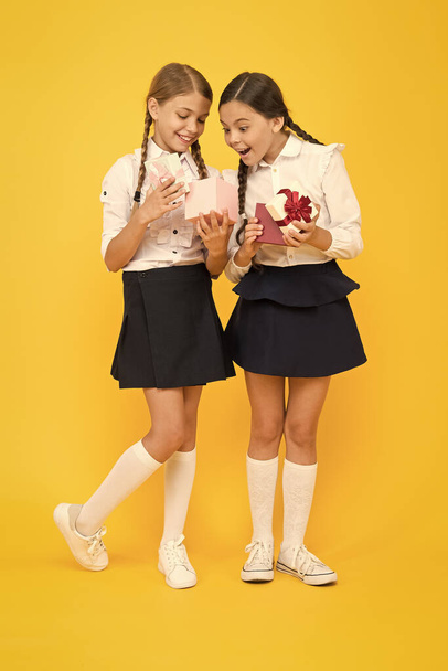 The best presents ever. Surprised little girls opening present boxes on yellow background. Happy children preparing school present for September 1. Small children getting birthday presents - Foto, imagen