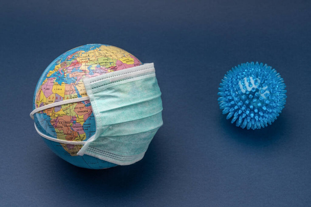 Medical mask put on globe globe with ball on blue background. - Fotó, kép