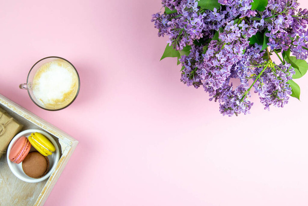 ミルクとギフト、ライラックの花とピンクのテーブルの上に甘いパステルフランスのマカロンとブラックコーヒーのカップ。透明感のあるトップビュー. - 写真・画像