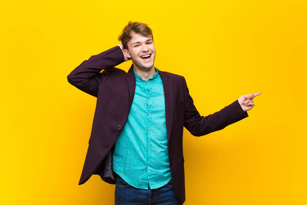 young blonde man laughing, looking happy, positive and surprised, realizing a great idea pointing to lateral copy space isolated against flat wall - Foto, immagini