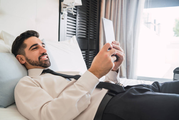 Portrait of young businessman lying on bed and using his digital tablet at the hotel room. Business travel concept. - Valokuva, kuva
